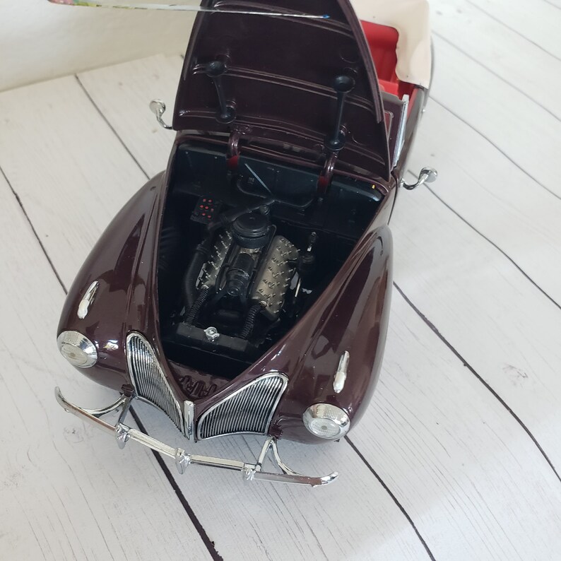 May include: A detailed model of a classic burgundy convertible car with the bonnet open, revealing the engine. The car has a cream-coloured top and chrome accents on the front bumper and grill. The interior is red.