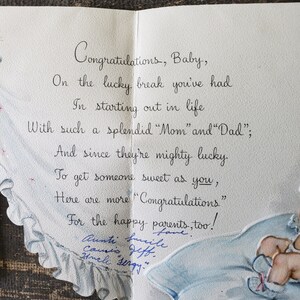 Op de afbeelding: Een vintage baby felicitatiekaart, opengeklapt om een handgeschreven bericht in elegant cursiefschrift te onthullen. De kaart heeft een blauw-wit ontwerp met een baby-illustratie. De tekst luidt "Gefeliciteerd, Baby".