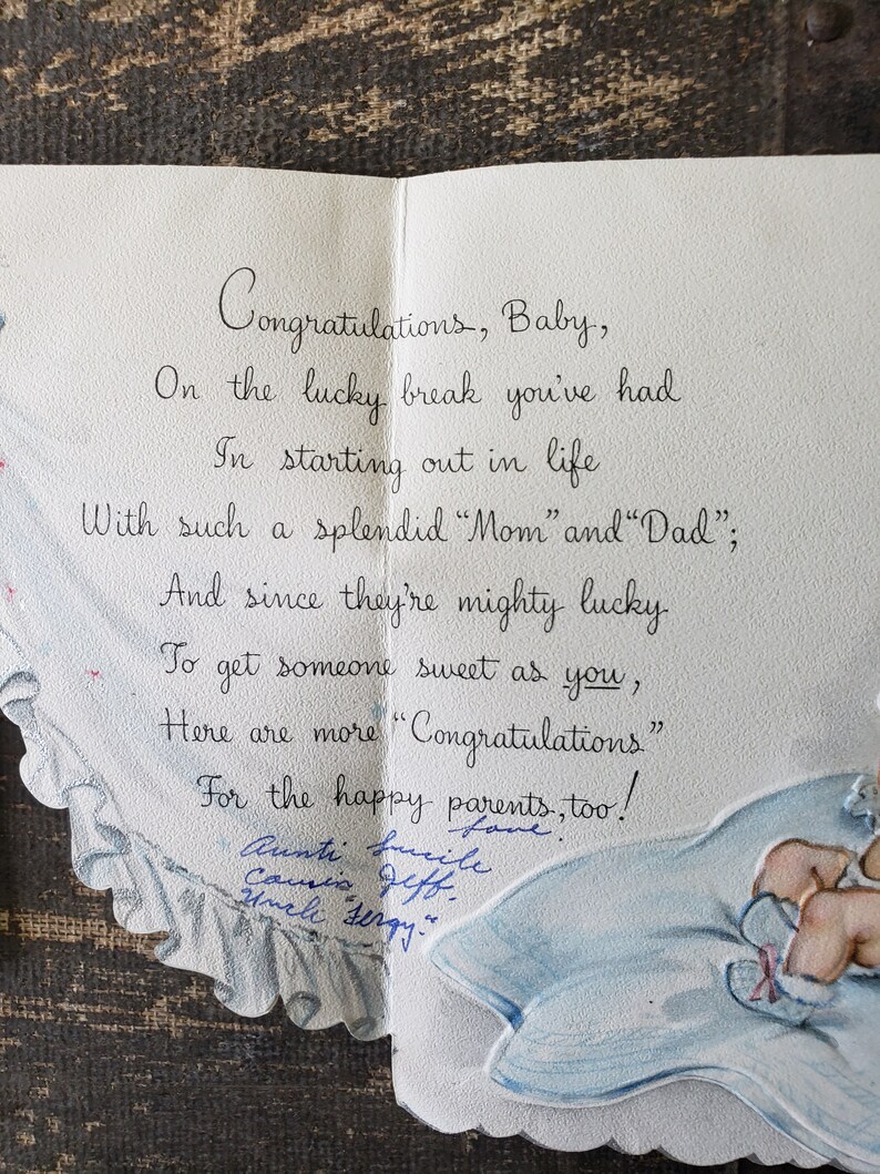 Op de afbeelding: Een vintage baby felicitatiekaart, opengeklapt om een handgeschreven bericht in elegant cursiefschrift te onthullen. De kaart heeft een blauw-wit ontwerp met een baby-illustratie. De tekst luidt "Gefeliciteerd, Baby".