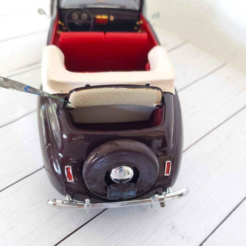 May include: A miniature brown convertible car with a spare tyre on the back. The car has a red interior, a cream seat, and chrome accents. The car is a vintage model.