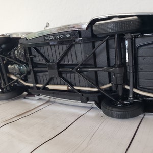 May include: Black die-cast model car with chrome detailing, visible undercarriage, and black tyres. The text "MADE IN CHINA" is visible on the underside. The car is on a light wood-grain surface.