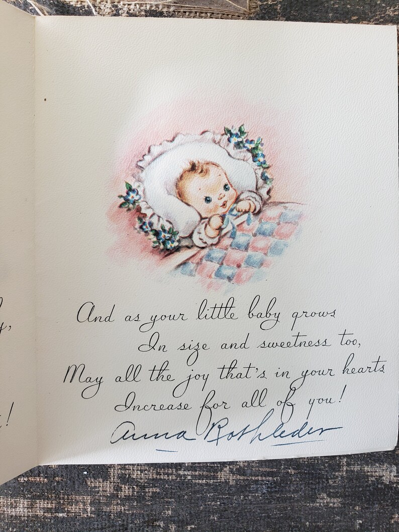 Op de afbeelding: Vintage baby wenskaart. De kaart toont een handgetekende illustratie van een baby in een witte muts, omringd door blauwe bloemen, op een roze en blauw geruite deken. De handgeschreven tekst luidt: "En als je kleine baby groeit..."