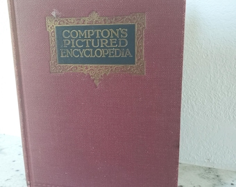 May include: A maroon-colored hardcover book with the title "COMPTON'S PICTURED ENCYCLOPEDIA" in gold lettering. The title is set within a decorative gold frame. The book's cover has a textured appearance.