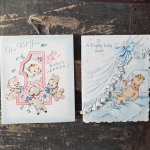 Op de afbeelding: Twee vintage baby-wenskaarten. E&eacute;n kaart zegt "Now That Your Baby's Arrived!" met een baby in een wieg en dierlijke illustraties. De andere kaart zegt "To A Mighty Lucky Baby" met een baby in een deken.