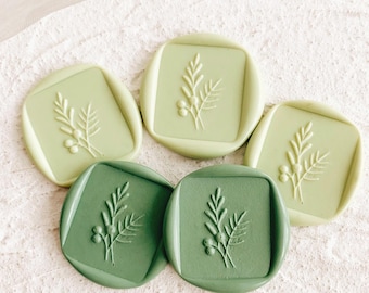 May include: Five green wax seals with a floral design. The seals are in various shades of green, from light to dark.