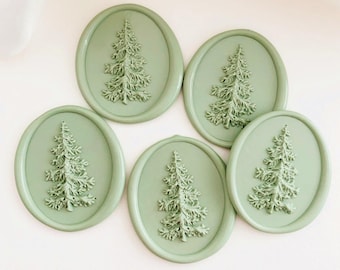 May include: Five oval-shaped, sage green wax seals with a raised fir tree design. The seals are arranged on a white surface, creating a cohesive and decorative set. The tree design is detailed and adds a touch of nature.