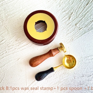 May include: A wax seal stamp set with a wooden handle, a gold-colored spoon, and a burner. The set includes a round, dark brown wax seal stamp with a gold-colored interior. The spoon has a gold bowl and a black handle. The text "Pack B" is visible.