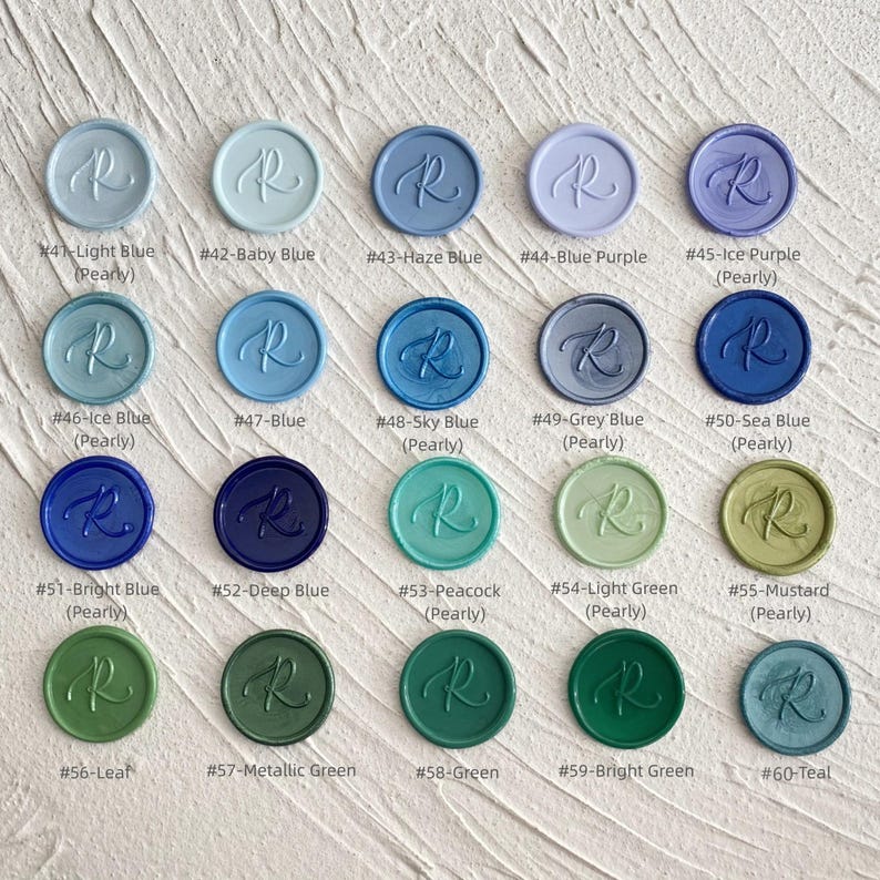 May include: A collection of wax seals in various colors, including light blue, baby blue, and teal. Each round seal features the letter "R" in a script font. The colors are labeled with names like "Haze Blue" and "Mustard".