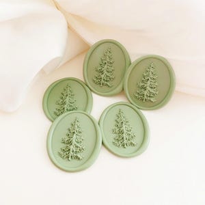 May include: Five sage green wax seals with a detailed tree design. The oval seals are arranged on a white surface with soft, flowing fabric in the background. The tree design is raised, creating a textured appearance.