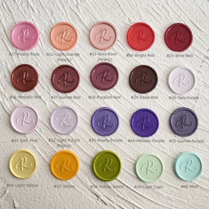 May include: A collection of colorful wax seals in various shades, including pink, orange, red, purple, yellow, and green. Each seal is round with the letter "R" in the center and a unique color name and number.