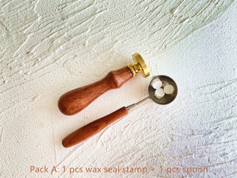 May include: A wax seal stamp with a wooden handle and a brass seal head, next to a small metal spoon holding three white wax beads. The text "Pack A: 1 pcs wax seal stamp + 1 pcs spoon" is at the bottom.