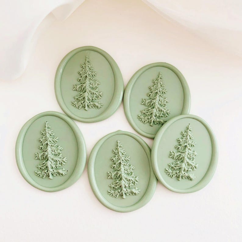 May include: Five oval-shaped, sage green wax seals with a raised fir tree design. The seals are arranged on a white surface, creating a cohesive and decorative set. The tree design is detailed and adds a touch of nature.