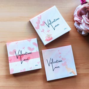 May include: Three pink and white Valentine's Day themed notepads with the text "Valentine Love" on each. The notepads have a watercolour background with pink hearts.