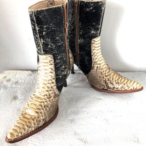 Könnte beinhalten: Ein Paar kniehohe Stiefel mit spitzer Zehenpartie. Die Stiefel haben ein Schlangenmuster in Beige und Braun mit schwarzen Akzenten am oberen Schaft. Sie haben einen Reißverschluss und einen Stiletto-Absatz.