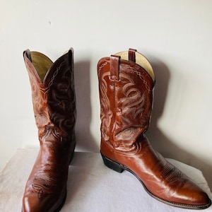 May include: A pair of brown leather cowboy boots. The boots have intricate stitching and a pointed toe. The leather has a glossy finish. The boots are a classic Western style.