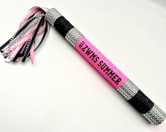 May include: A decorative baton with a pink, black, and silver design. The baton has a pink central section with the text "ZWMS SUMMER 2023". The handle is black and silver with rhinestones. A tassel of ribbons in pink, black, and silver adorns the top.
