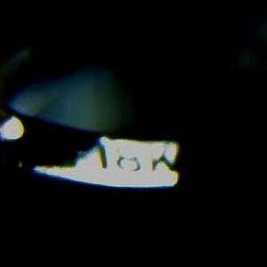 May include: A blurry, close-up image of a white object with the text "10A" on it, set against a dark background. The object's shape is indistinct due to the focus and lighting.