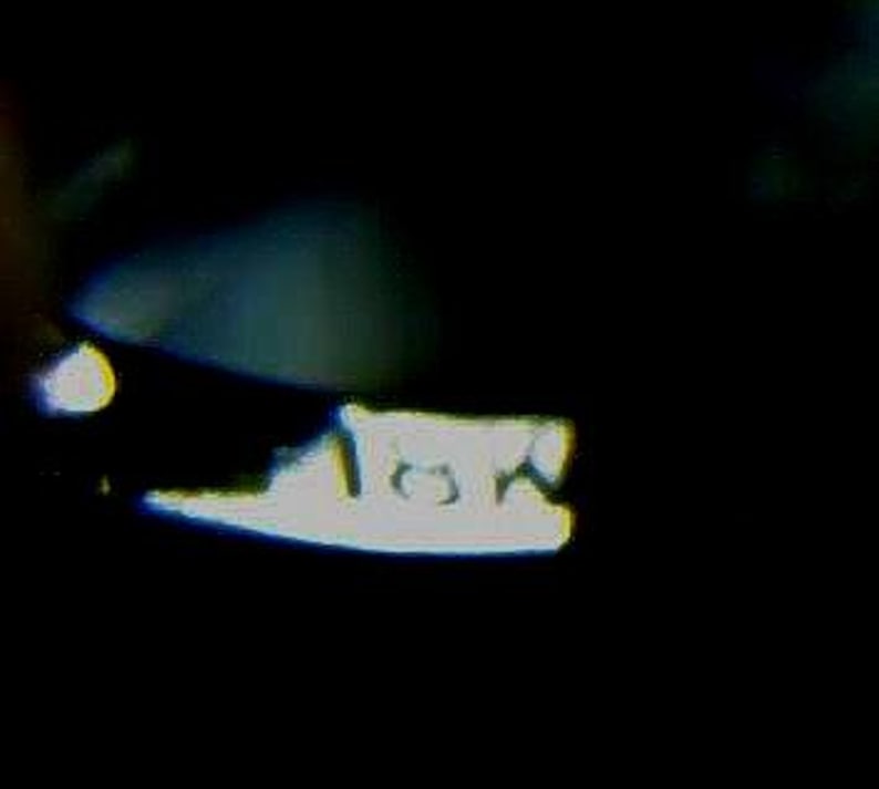 May include: A blurry, close-up image of a white object with the text "10A" on it, set against a dark background. The object's shape is indistinct due to the focus and lighting.