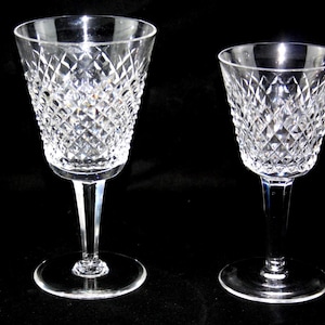 May include: Two clear crystal wine glasses with diamond-cut patterns. The glasses have a classic design, featuring a stemmed base and a wide bowl. The background is a solid black, highlighting the clarity and detail of the glassware.