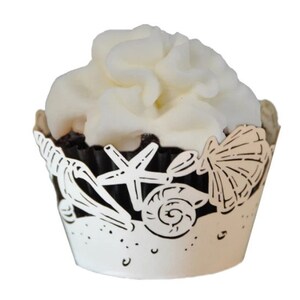 Op de afbeelding: Witte cupcake-verpakking met een ontwerp van een schelp, een zeester en een schelp. De verpakking is gemaakt van papier en heeft een delicate, kant-achtige uitstraling.