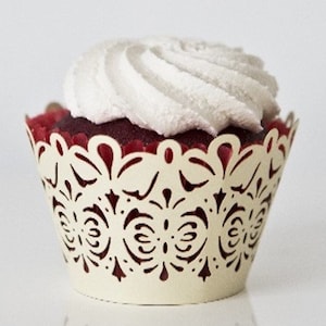 Puede incluir: Un cupcake blanco con glaseado de terciopelo rojo y un remolino de crema de mantequilla blanca, decorado con un delicado envoltorio de cupcake de encaje marfil con un diseño de mariposa.