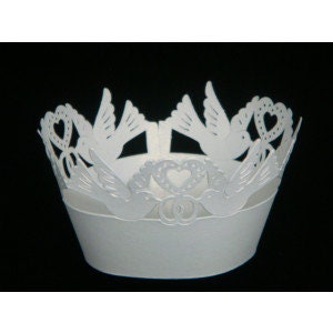 May include: White cupcake wrapper with a delicate design of doves and hearts. The doves are in flight and the hearts have a dotted pattern. The wrapper is perfect for a wedding or anniversary celebration.