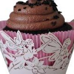 May include: A chocolate cupcake with chocolate frosting and sprinkles sits in a pink and white fairy-themed cupcake liner. The liner features a cut-out design of fairies and flowers.