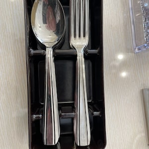 Peut inclure: Un porte-couteaux en plastique noir avec une fourchette et une cuillère en argent à l'intérieur.
