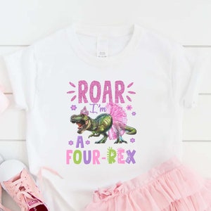 May include: White t-shirt with a colorful graphic that reads "ROAR I'm A FOUR-REX". The design features a cartoon dinosaur wearing a tutu and crown. A pink tulle skirt and pink shoes are also in the image.