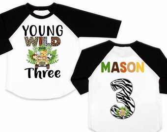 May include: White and black baseball tee shirt with a jungle animal theme. The front of the shirt says "Young Wild and Three" with a jeep full of animals. The back of the shirt says "Mason" with a zebra patterned number 3.