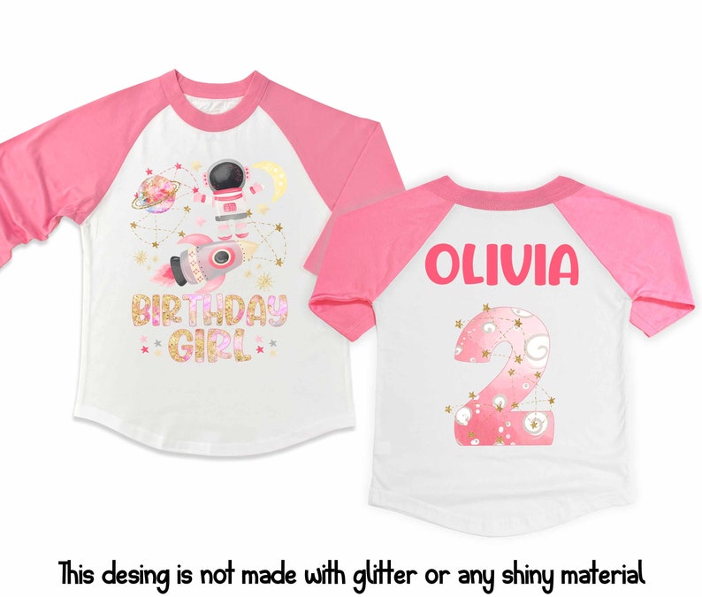 May include: White and pink raglan-style birthday shirt. The front features an astronaut, rocket, and the words "BIRTHDAY GIRL". The back has the name "OLIVIA" and a number 2. The design is not made with glitter or shiny material.