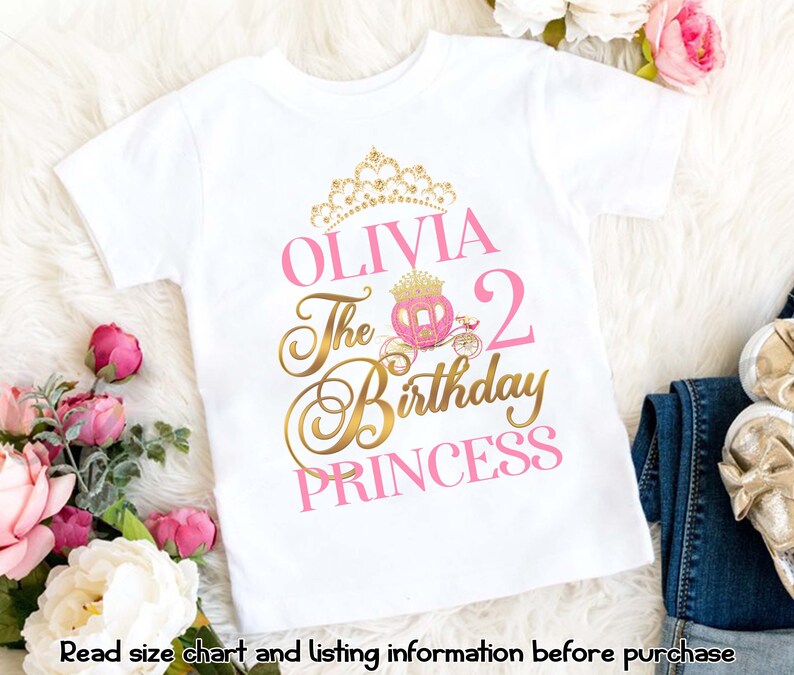 Pu&ograve; includere: Maglietta bianca con un design rosa e oro. Il design presenta una corona, una carrozza e il testo "Olivia The 2nd Birthday Princess".