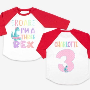 May include: Two white and red baseball shirts with a dinosaur design. One shirt says "Roar I'm a Three Rex" and the other says "Charlotte 3".
