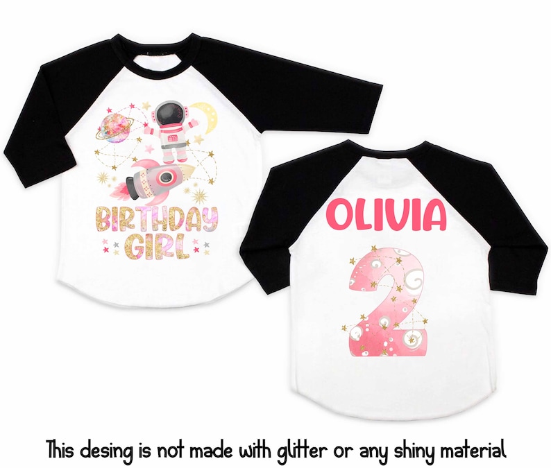May include: White and black raglan-style birthday shirt. The front features an astronaut, rocket, and the words "BIRTHDAY GIRL." The back displays the name "OLIVIA" and a pink number 2. The design is not made with glitter.
