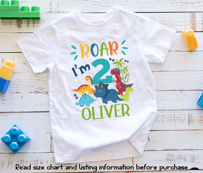 May include: White t-shirt with a dinosaur theme. The shirt says "Roar I'm 2 Oliver" with a large number 2 and colorful dinosaurs.