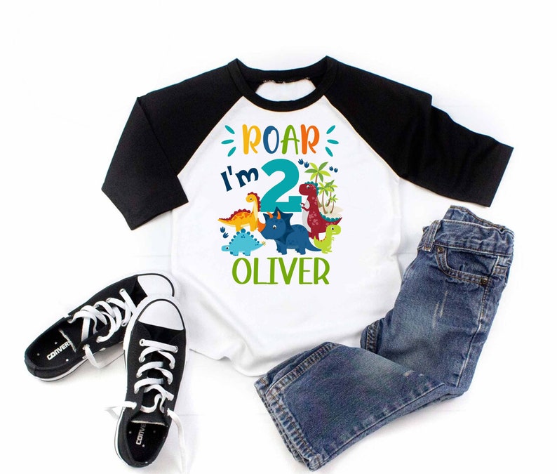 May include: A white and black baseball tee shirt with a dinosaur graphic and the text "Roar I'm 2 Oliver".