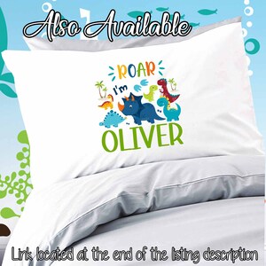 May include: White pillowcase with a dinosaur design. The design features a blue dinosaur with the text "Roar I'm Oliver" in green, blue, orange, and yellow.
