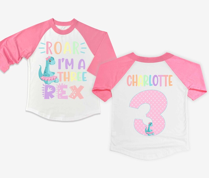 May include: A white and pink baseball style t-shirt with a rainbow dinosaur graphic and the text "Roar I'm a Three Rex". The back of the shirt has a pink polka dot number 3 with a dinosaur graphic and the name "Charlotte" in rainbow letters.