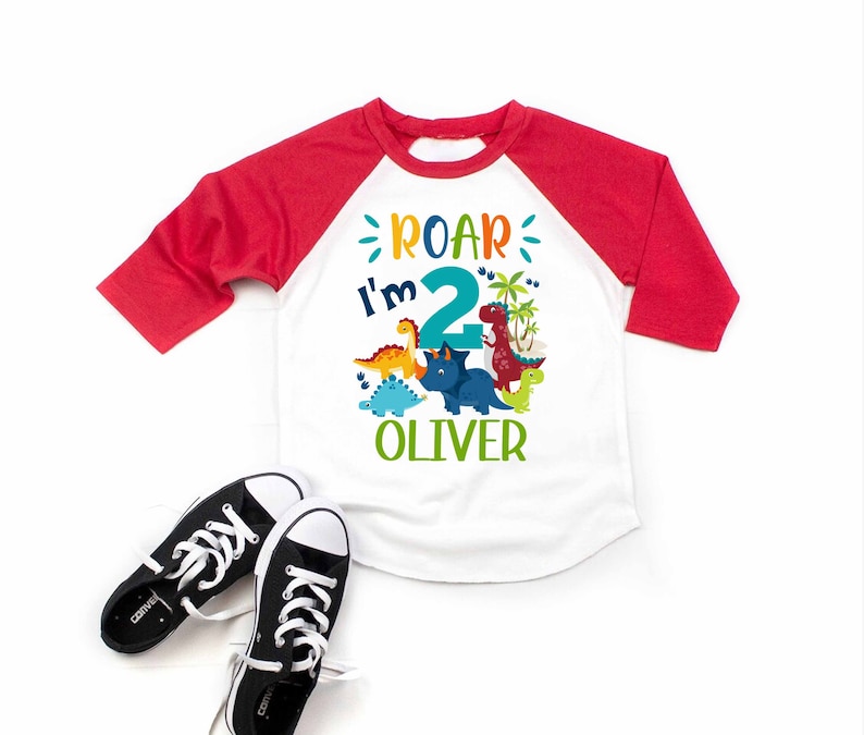May include: A white and red baseball tee shirt with a dinosaur theme. The shirt says "Roar I'm 2 Oliver".