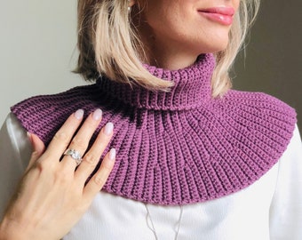 May include: A close-up of a purple crocheted cowl neck warmer. The cowl is made with a simple stitch and has a ruffled edge.