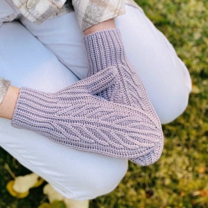 Könnte beinhalten: Ein Paar gestrickte Fäustlinge in helllila. Die Fäustlinge haben ein strukturiertes Muster und sind übereinander gelegt.