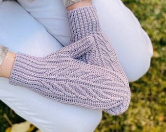 Könnte beinhalten: Ein Paar gestrickte Fäustlinge in helllila. Die Fäustlinge haben ein strukturiertes Muster und sind übereinander gelegt.