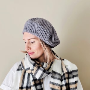 Peut inclure: Une femme portant un béret en tricot gris et une écharpe à carreaux blancs et noirs.
