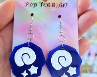 Pode incluir: Um par de brincos azuis e brancos com um design de espiral e estrela. Os brincos são presos por um gancho prateado. Os brincos estão em um cartão que diz "Pop Twilight".
