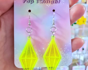 Pode incluir: Brincos em forma de diamante amarelo néon com ganchos prateados, exibidos em um cartão que diz "Pop Twilight". Os brincos são geométricos e chamativos. Mais joias são visíveis no fundo.
