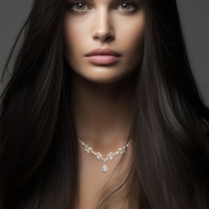 May include: A woman with long, dark hair wearing a gold necklace with floral and teardrop-shaped pendant. The necklace is centered on the chest. The background is a solid grey.