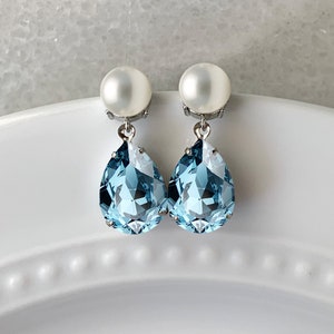 A close up of a pair of earrings with a pearl post and aquamarine crystals. The crystal drops are teardrop shaped and measure 14mm x 10mm