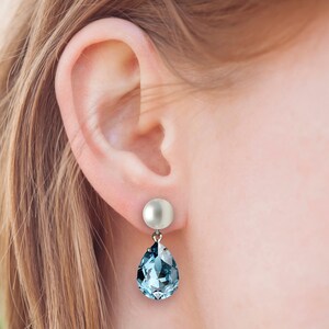 A model wearing an earring with a pearl post and aquamarine crystal pear shaped drop