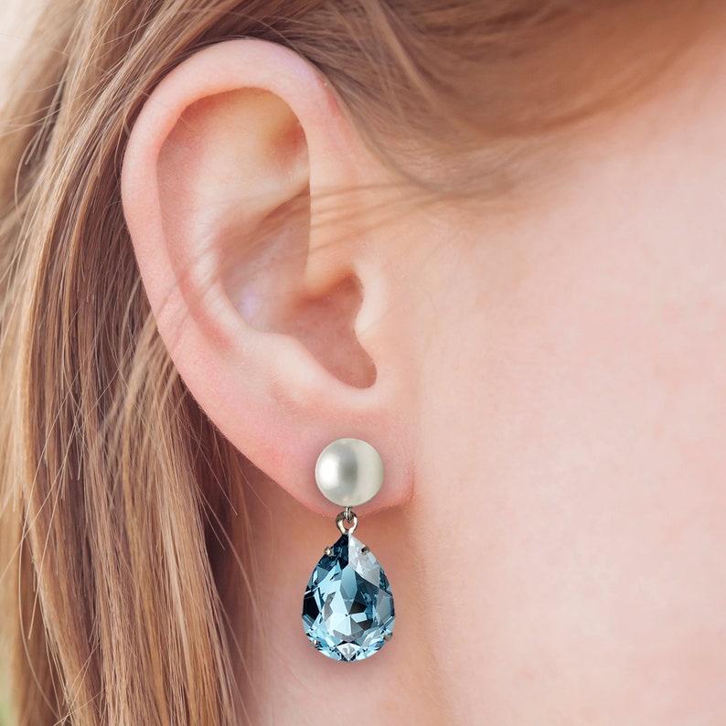 A model wearing an earring with a pearl post and aquamarine crystal pear shaped drop