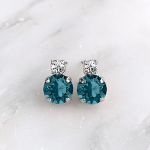 May include: A pair of silver earrings with a teal blue gemstone and a smaller clear gemstone.